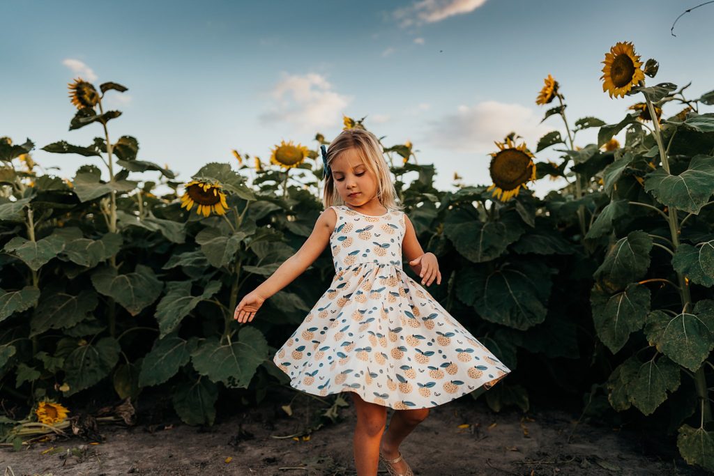 girl spinning in dress in sunflower field 