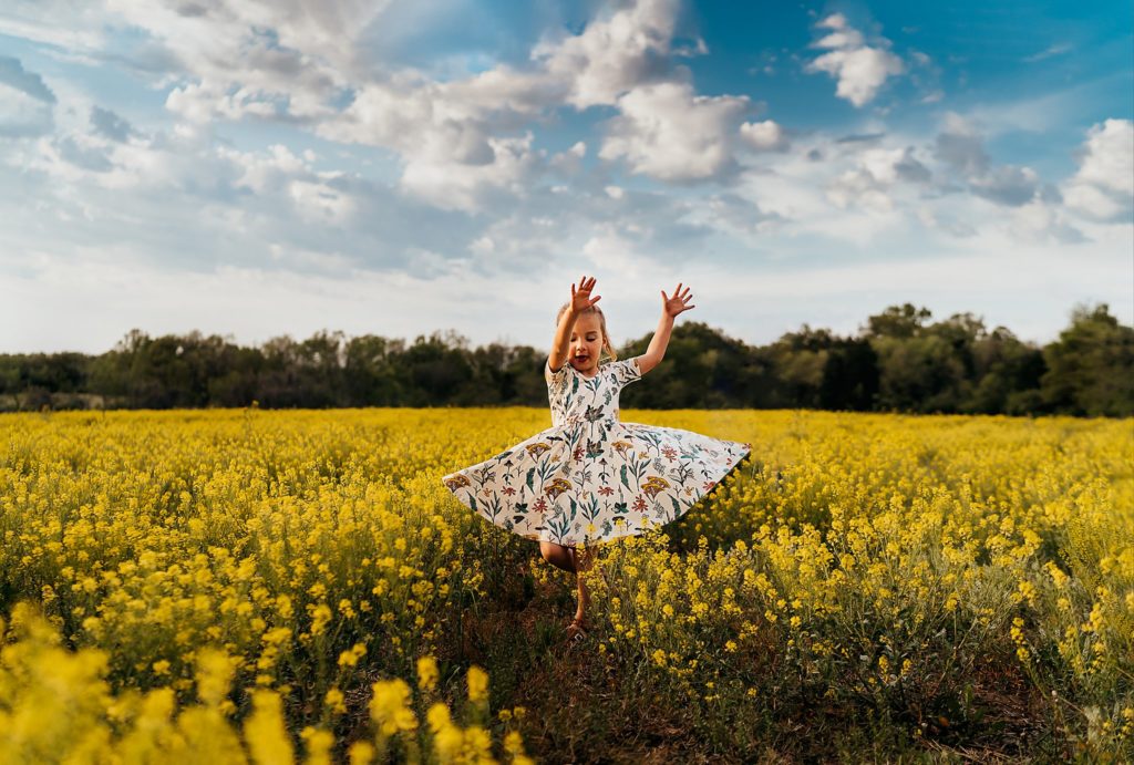 girl spinning in yellow flower field 